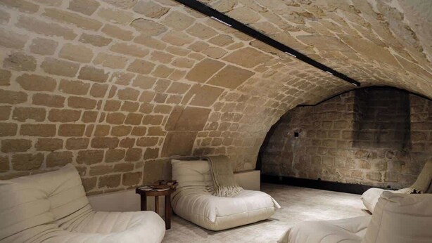 A stone-walled room with three cushioned seating areas and a small table. - An Exceptional 3-BR/3Ba with Services - Le Marais (Paris)