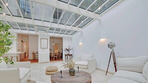 A spacious living area with a high ceiling and skylight, featuring a round wooden coffee table, white sofas, and a tripod lamp. - A Breathtaking 2-BR/1Ba - Gobelins (Paris)