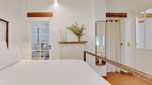 A bedroom with a large bed, a wooden headboard, a window, a radiator, a mirror, and a door. - A Breathtaking 2-BR/1Ba - Gobelins (Paris)