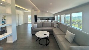 A spacious living area with a large sectional sofa, a round coffee table, and a kitchen in the background. - Ishem • Penthouse • Free Wi-Fi • 2 Balconies • Green View • Garden •Pet-Friendly (Ishëm)