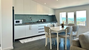 A modern kitchen with white cabinets, a black countertop, and a view of the landscape through large windows. - Ishem • Penthouse • Free Wi-Fi • 2 Balconies • Green View • Garden •Pet-Friendly (Ishëm)