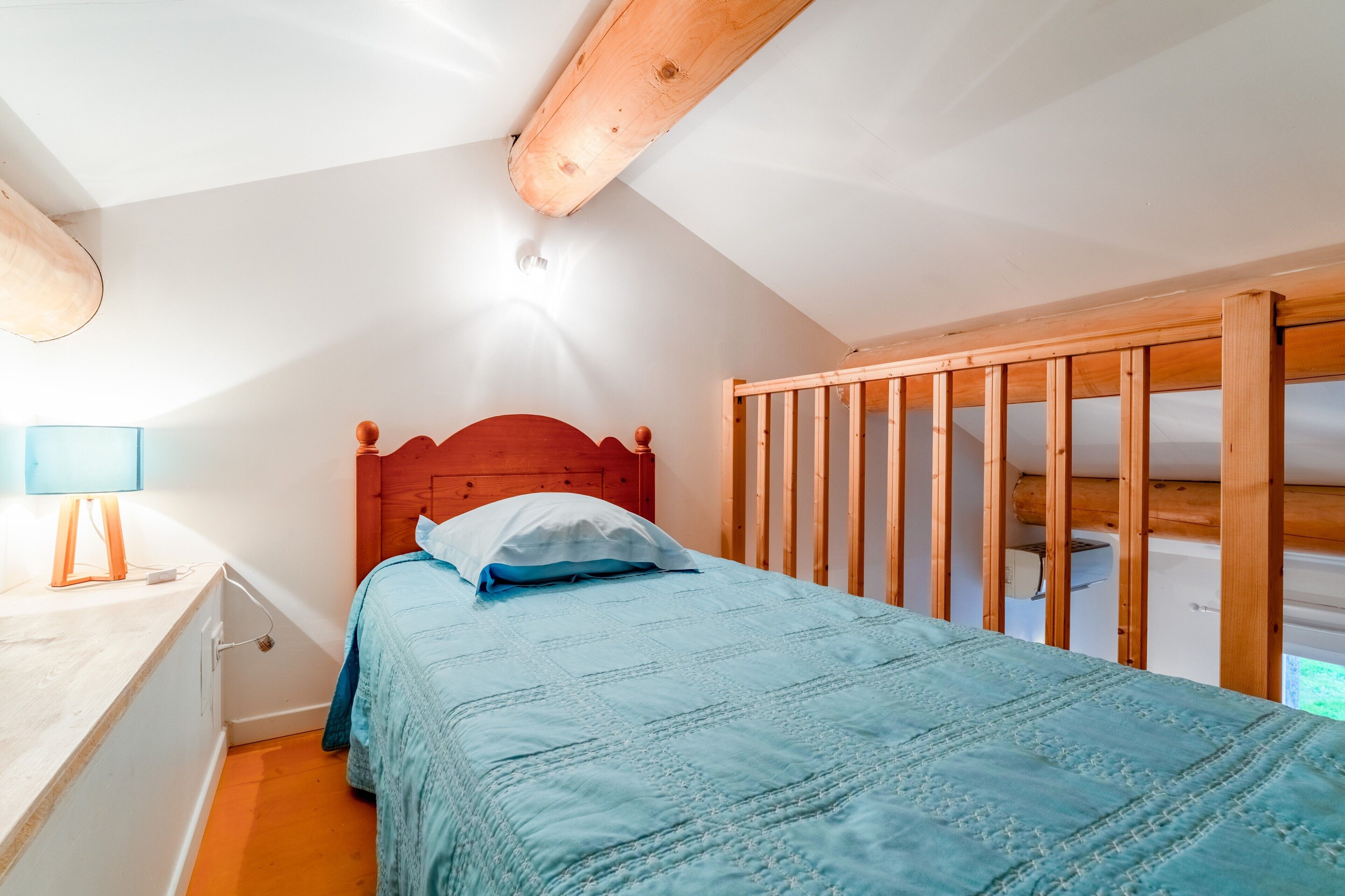 Une chambre avec une tête de lit en bois, un lit recouvert d’une couette bleue, une table de chevet avec une lampe et une cloison en bois.