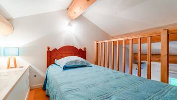 Une chambre avec une tête de lit en bois, un lit recouvert d’une couette bleue, une table de chevet avec une lampe et une cloison en bois.