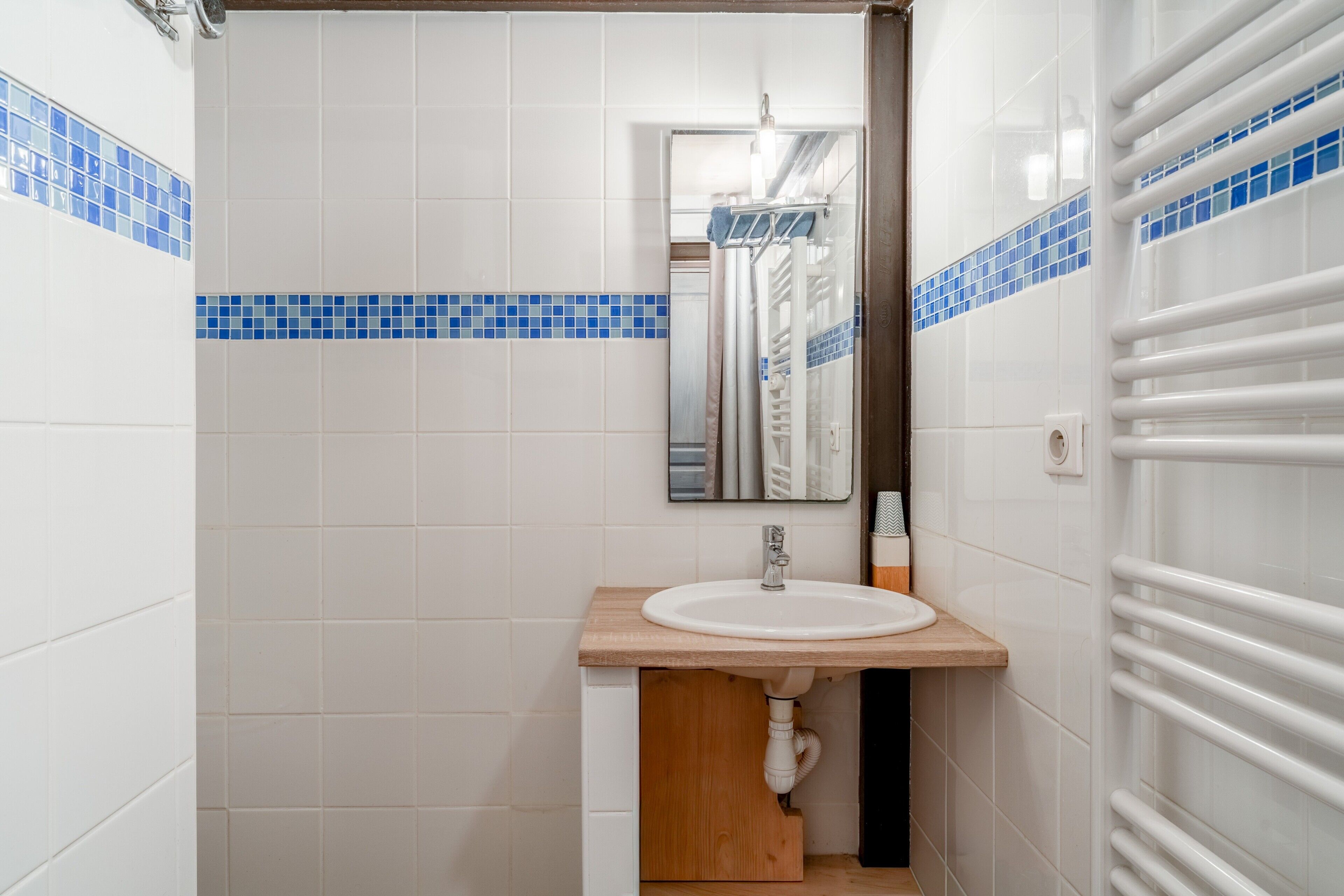 A bathroom with white tiles, a wooden sink, and a towel rack.