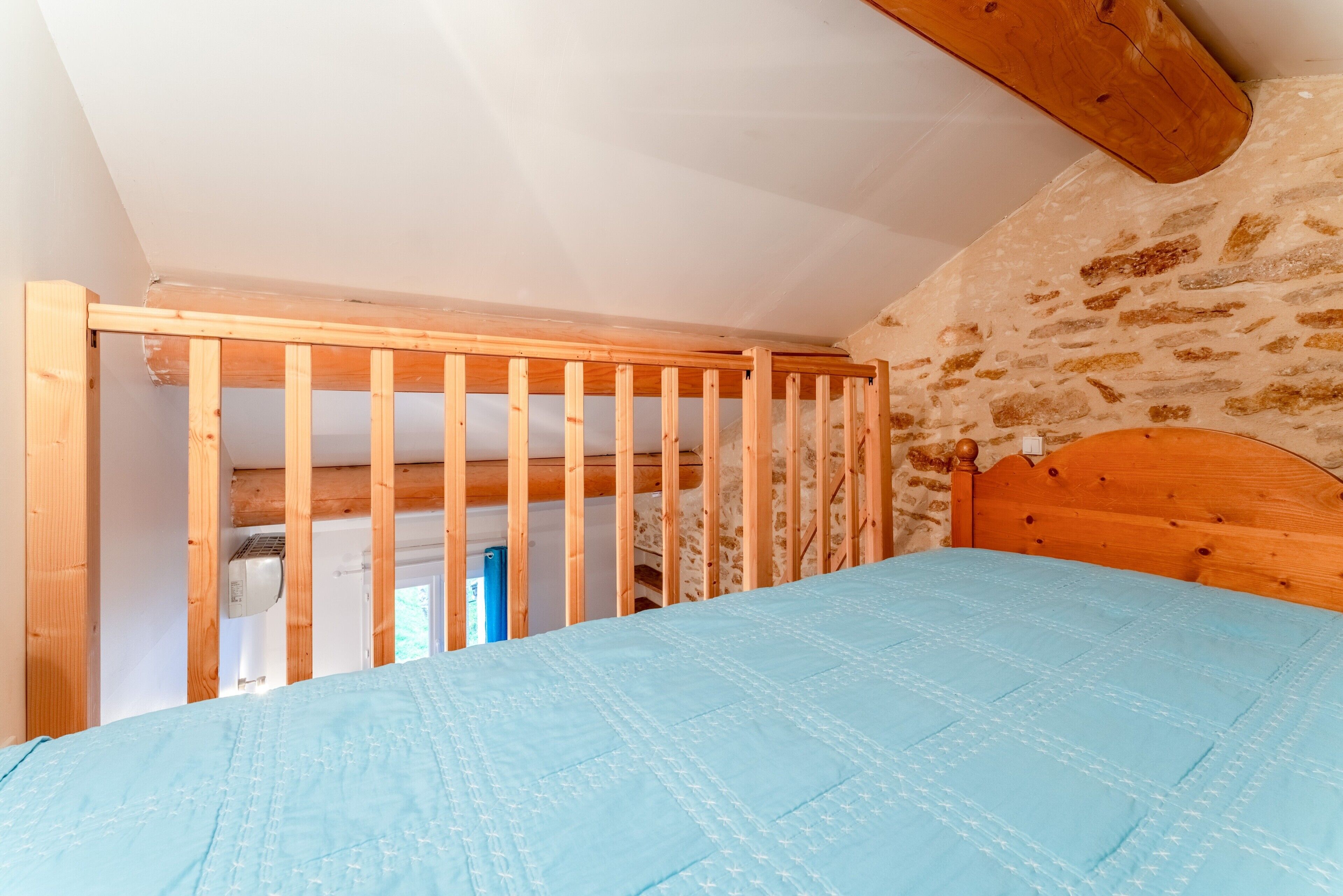 A bedroom with a wooden headboard, a blue bedspread, and a stone wall.