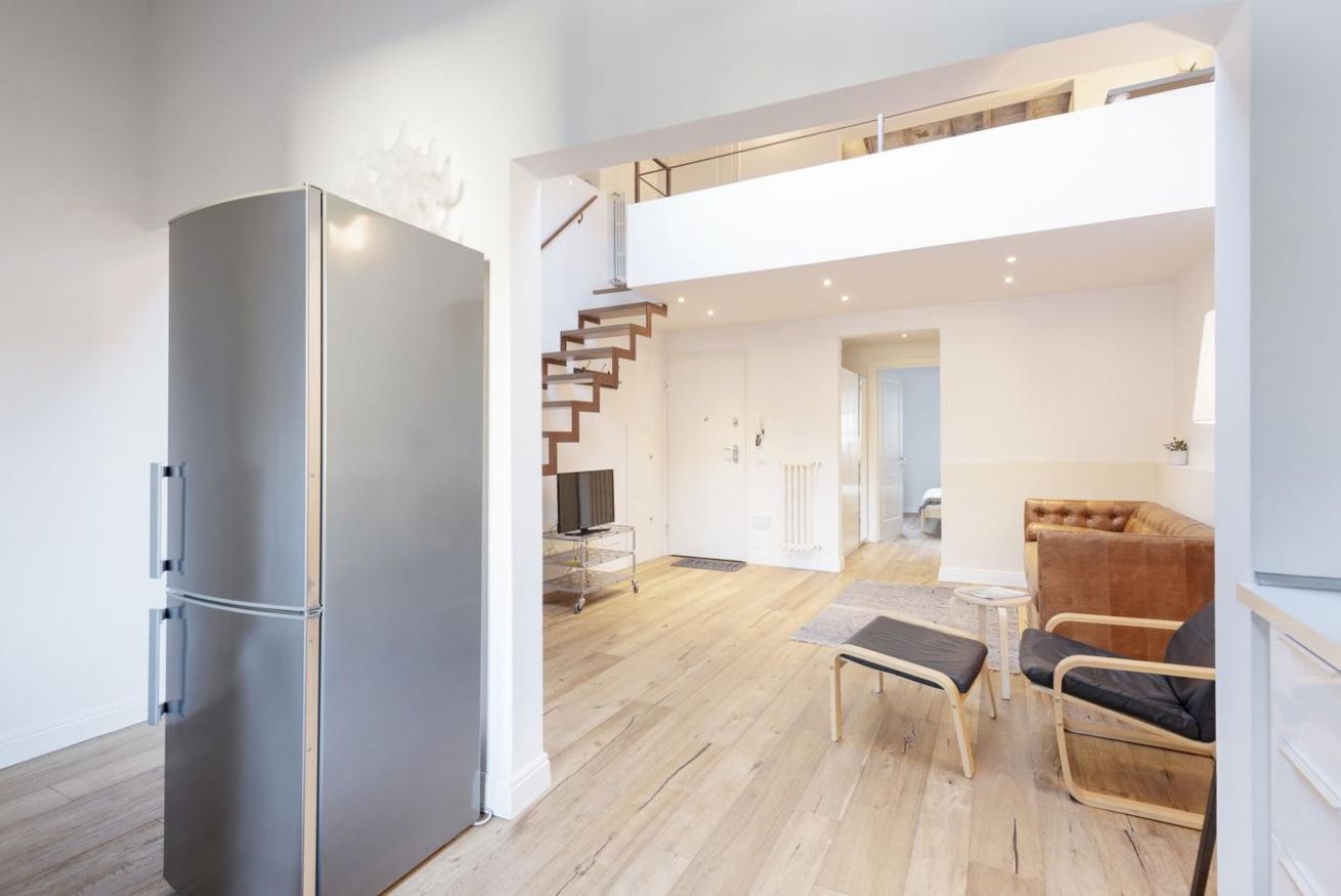 A modern kitchen with a large refrigerator, a dining area with a table and chairs, and a staircase leading to an upper level.