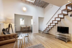 Ein modernes Wohnzimmer mit einer Holztreppe, einem Fernseher auf einem Wagen und einem Essbereich.