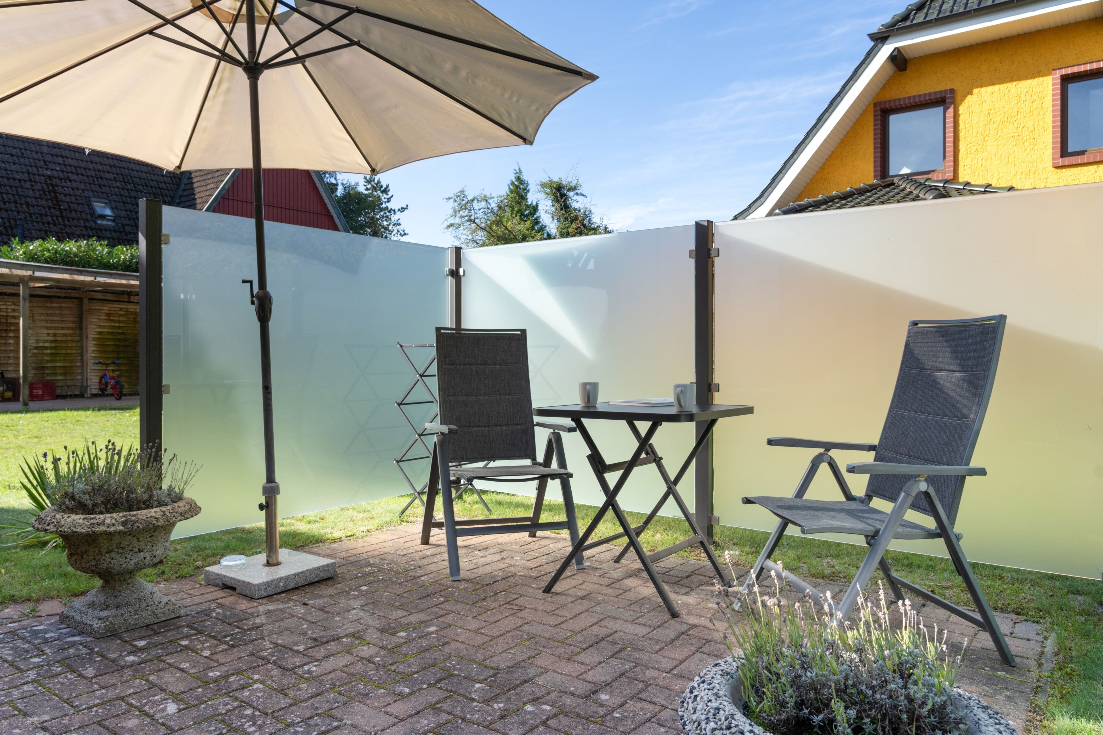 Eine Terrasse mit Tisch, Stühlen, einem großen Sonnenschirm und einem Sichtschutz.