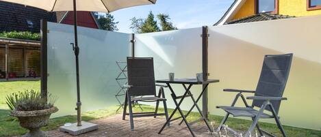 Une terrasse avec une table et des chaises, un grand parasol et un écran pour préserver l’intimité.