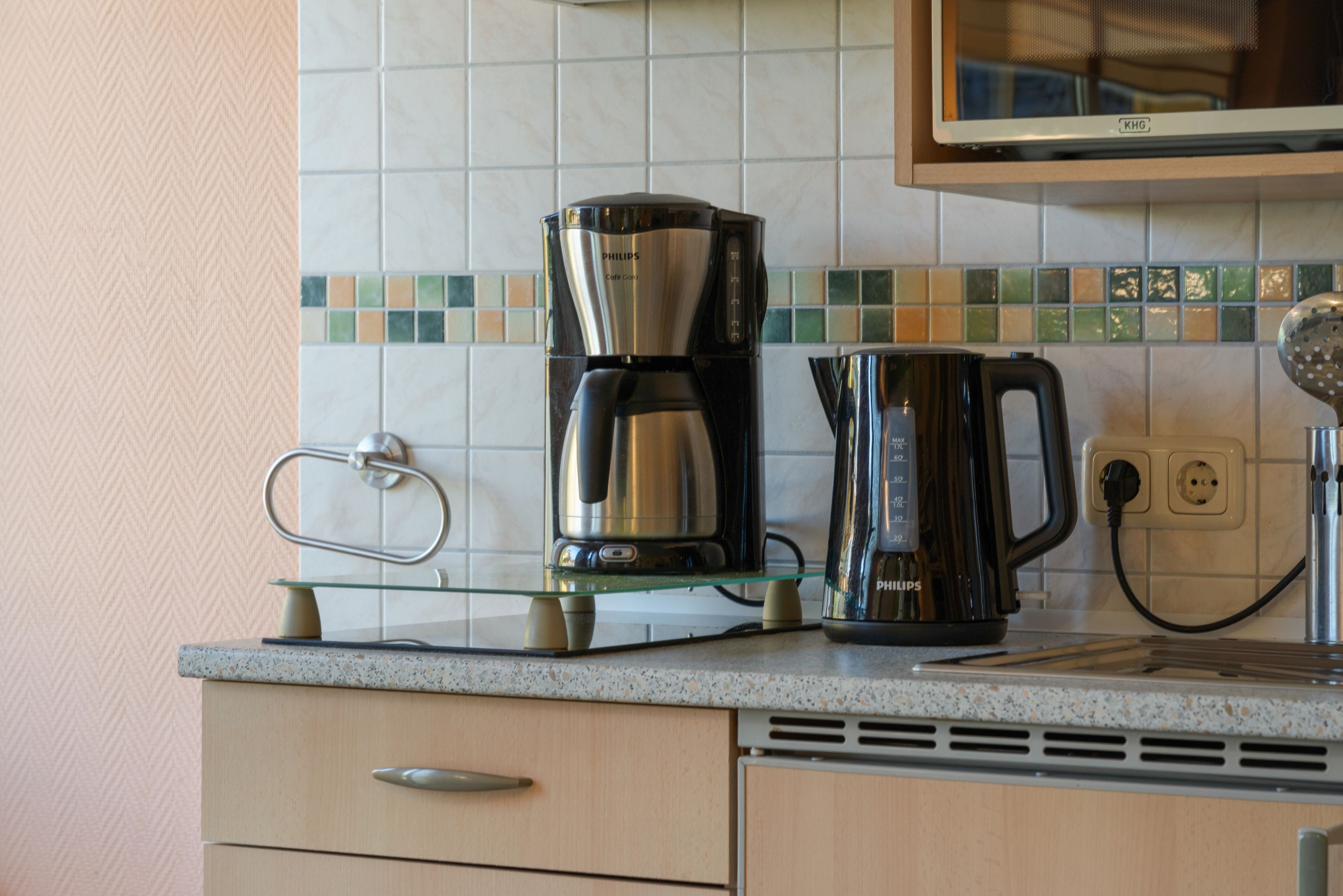 Eine Küche mit einer Kaffeemaschine, einem Wasserkocher und einer Mikrowelle auf der Arbeitsfläche.