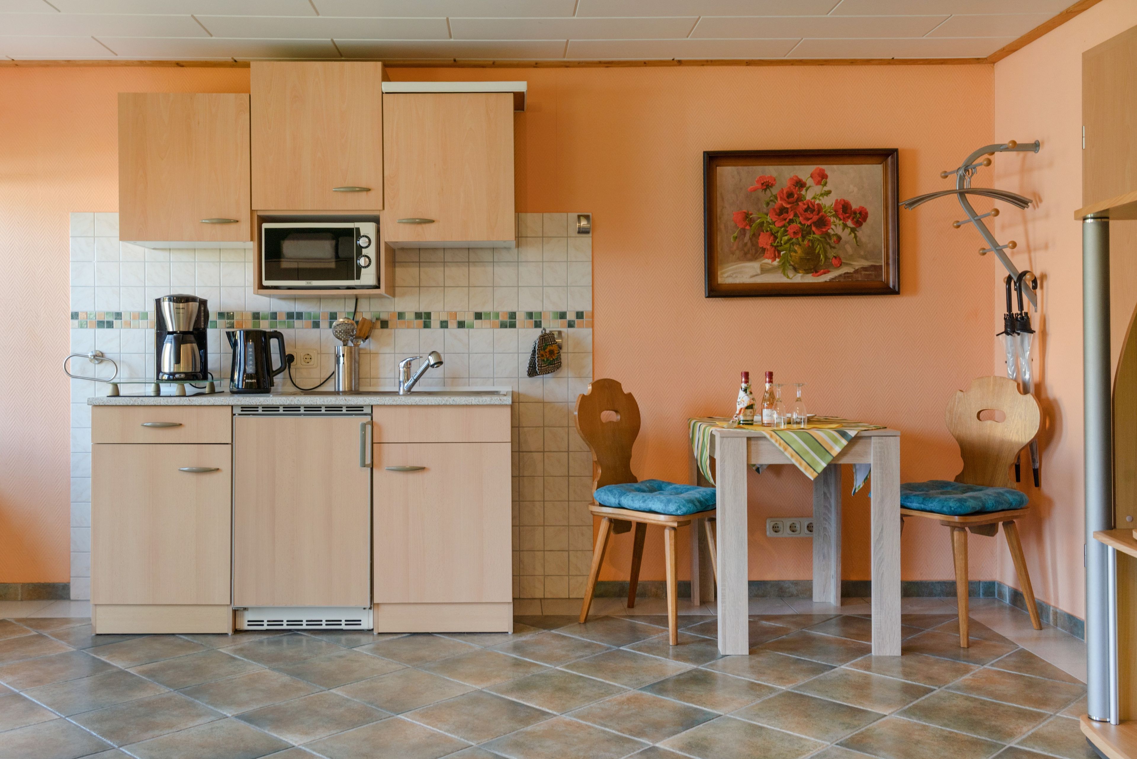 Cozinha compacta com armários de madeira, micro-ondas, cafeteira e área de refeições com mesa e cadeiras.