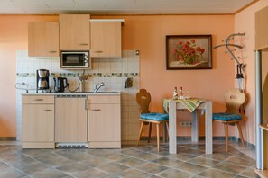Cocina compacta con armarios de madera, microondas, cafetera y zona de comedor con mesa y sillas.
