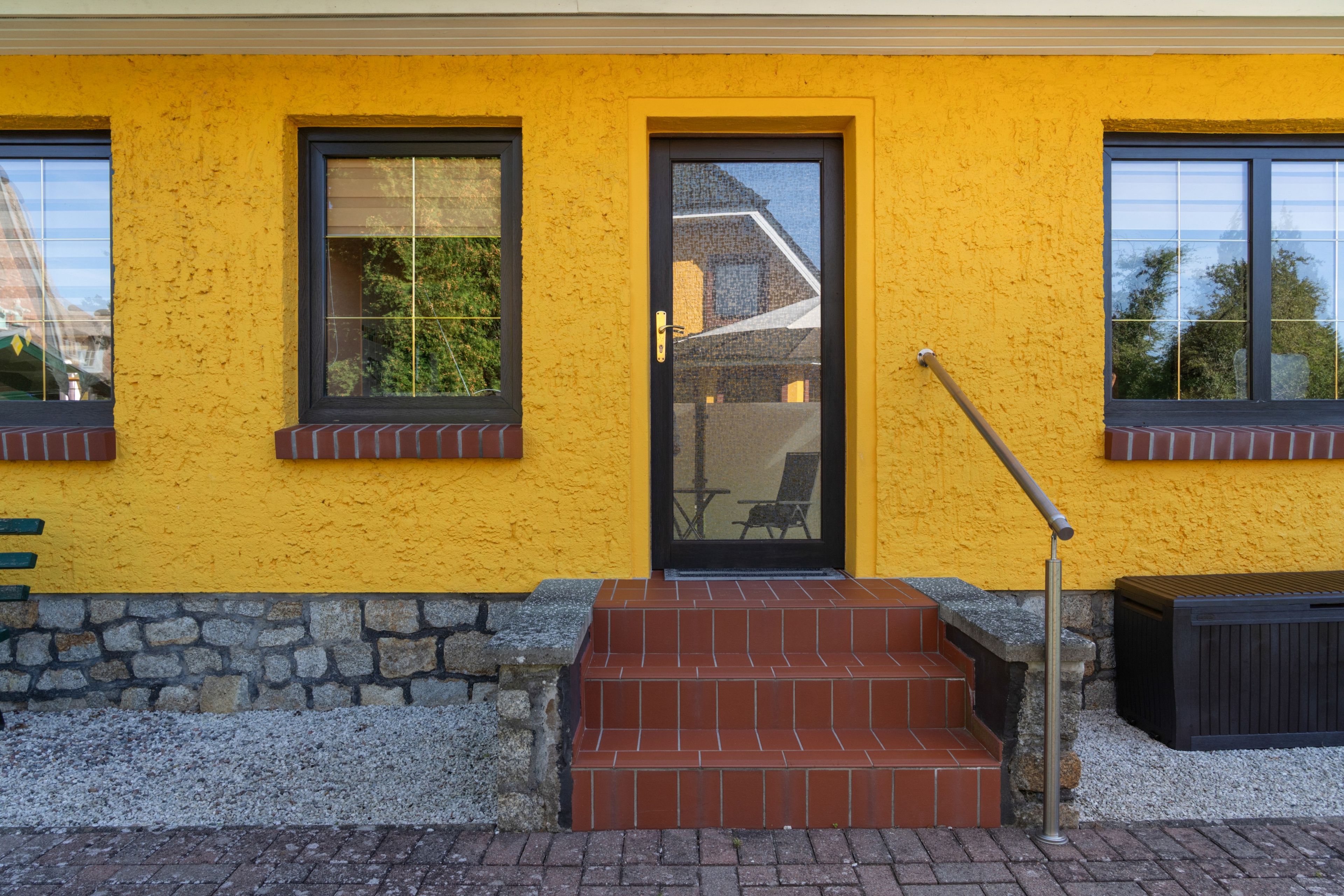 A building with a yellow exterior, a black door, and a set of stairs leading to a small porch area.