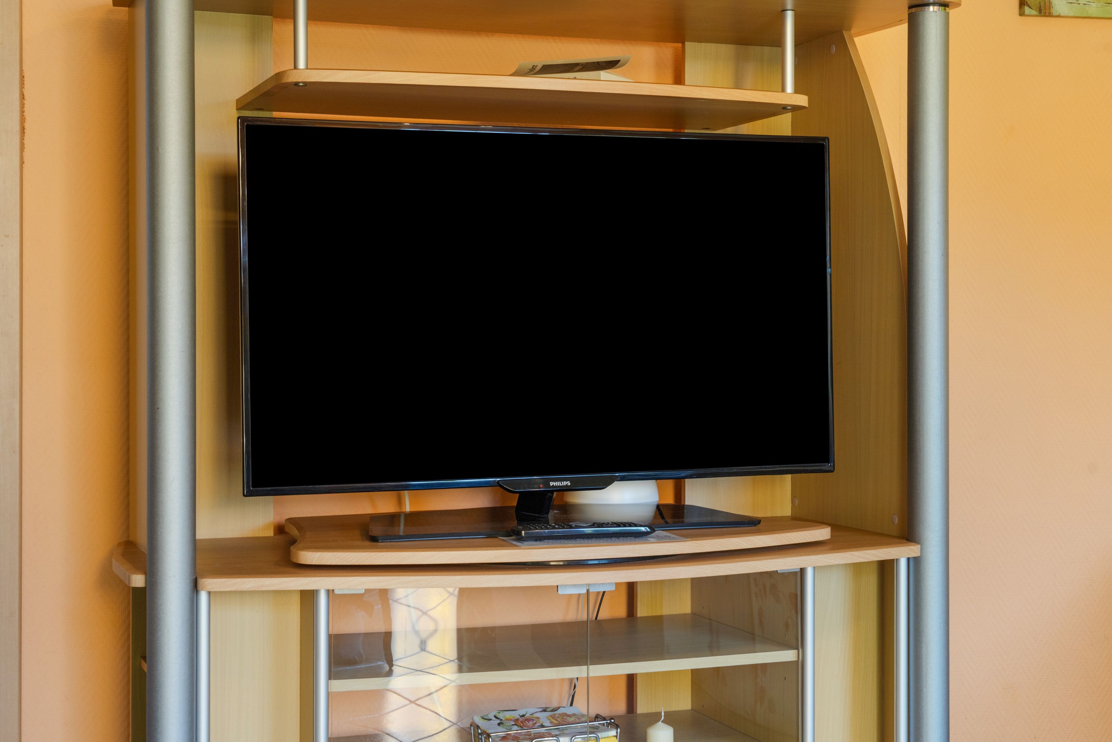 Ein Fernseher auf einem hölzernen Ständer mit Metallrahmen, platziert in einem Raum mit Holzwänden und Fliesenboden.