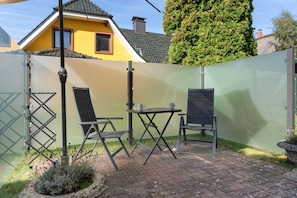 Un área de estar al aire libre con dos sillas y una mesa, delimitada por una cerca verde.