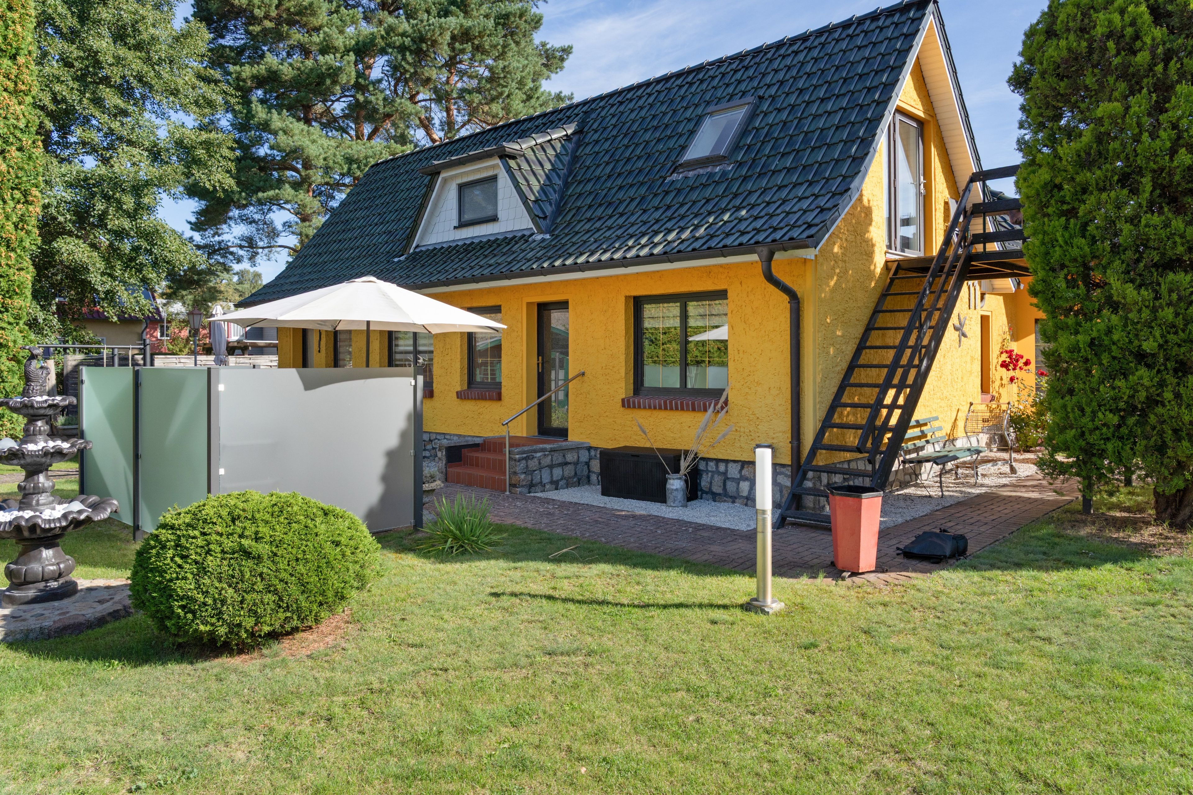 Una casa amarilla con techo oscuro, un pequeño porche y una escalera que lleva a un segundo piso.
