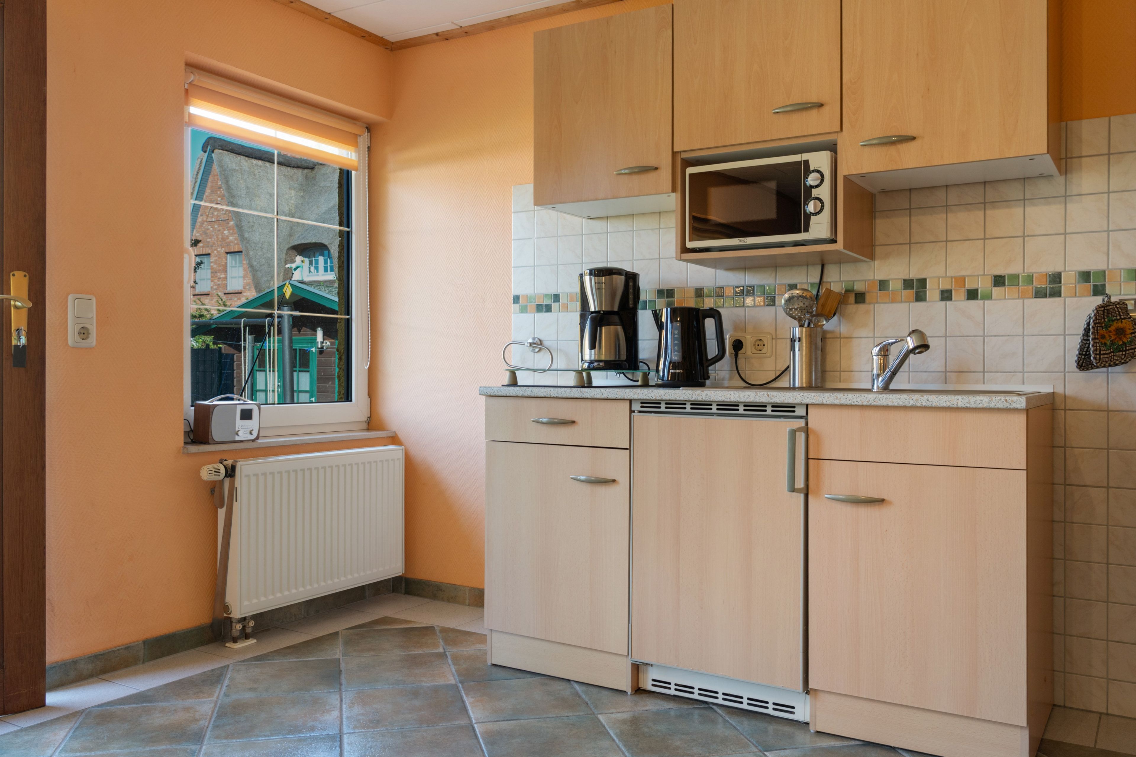 Eine kleine Küche mit Mikrowelle, Kaffeemaschine und einem Fenster mit Jalousien.