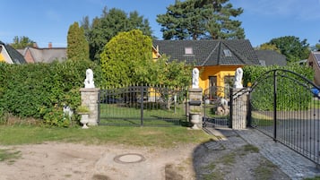 En grind markerar ingången, och en stenlagd gång leder fram till en byggnad med ett tak täckt av tegelpannor.