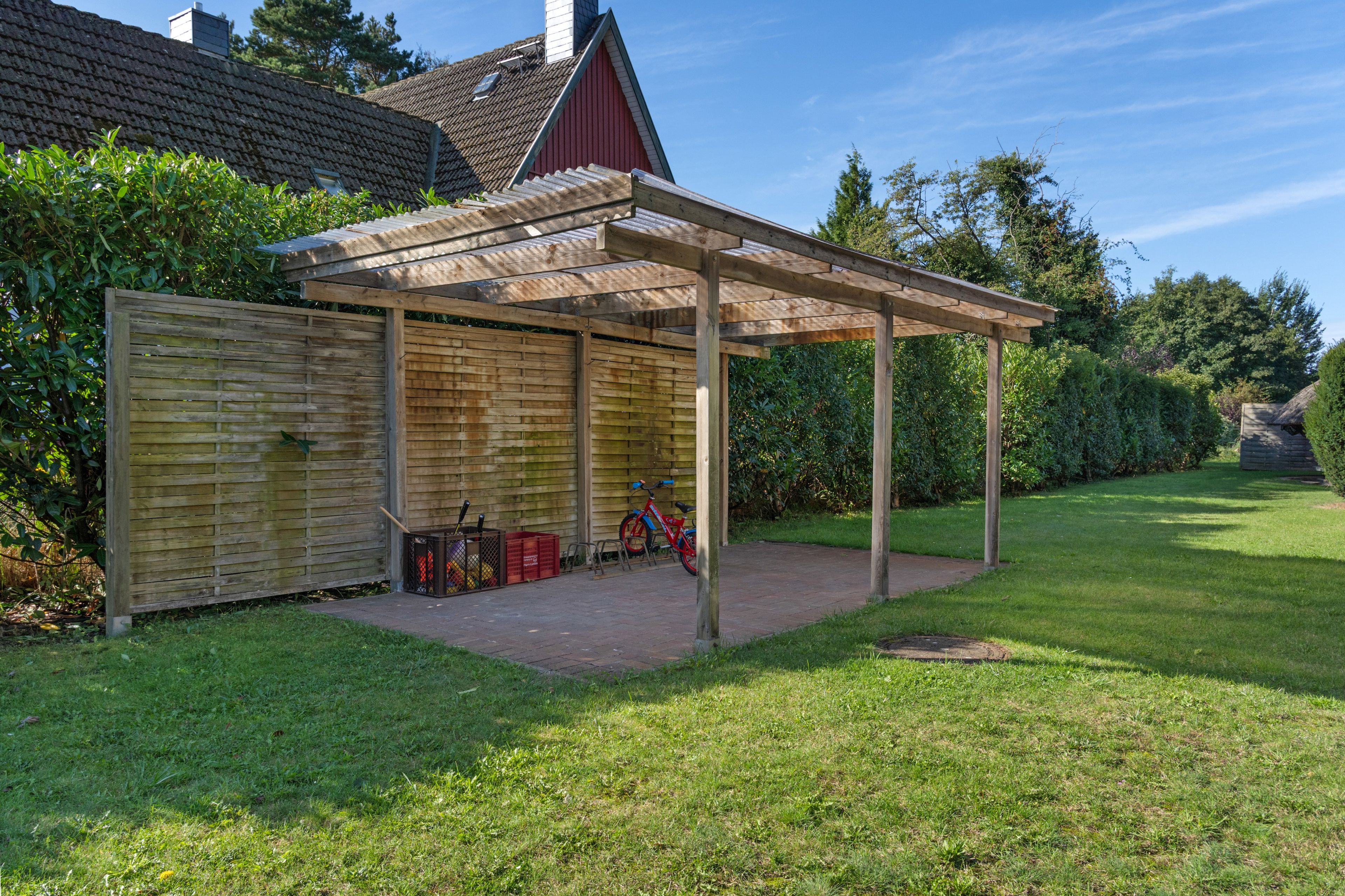 Ein überdachter Patio-Bereich mit Holzfence, einem roten Fahrrad und einem roten Gebäude im Hintergrund.