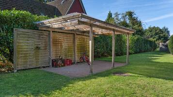 Ein überdachter Patio-Bereich mit Holzfence, einem roten Fahrrad und einem roten Gebäude im Hintergrund.