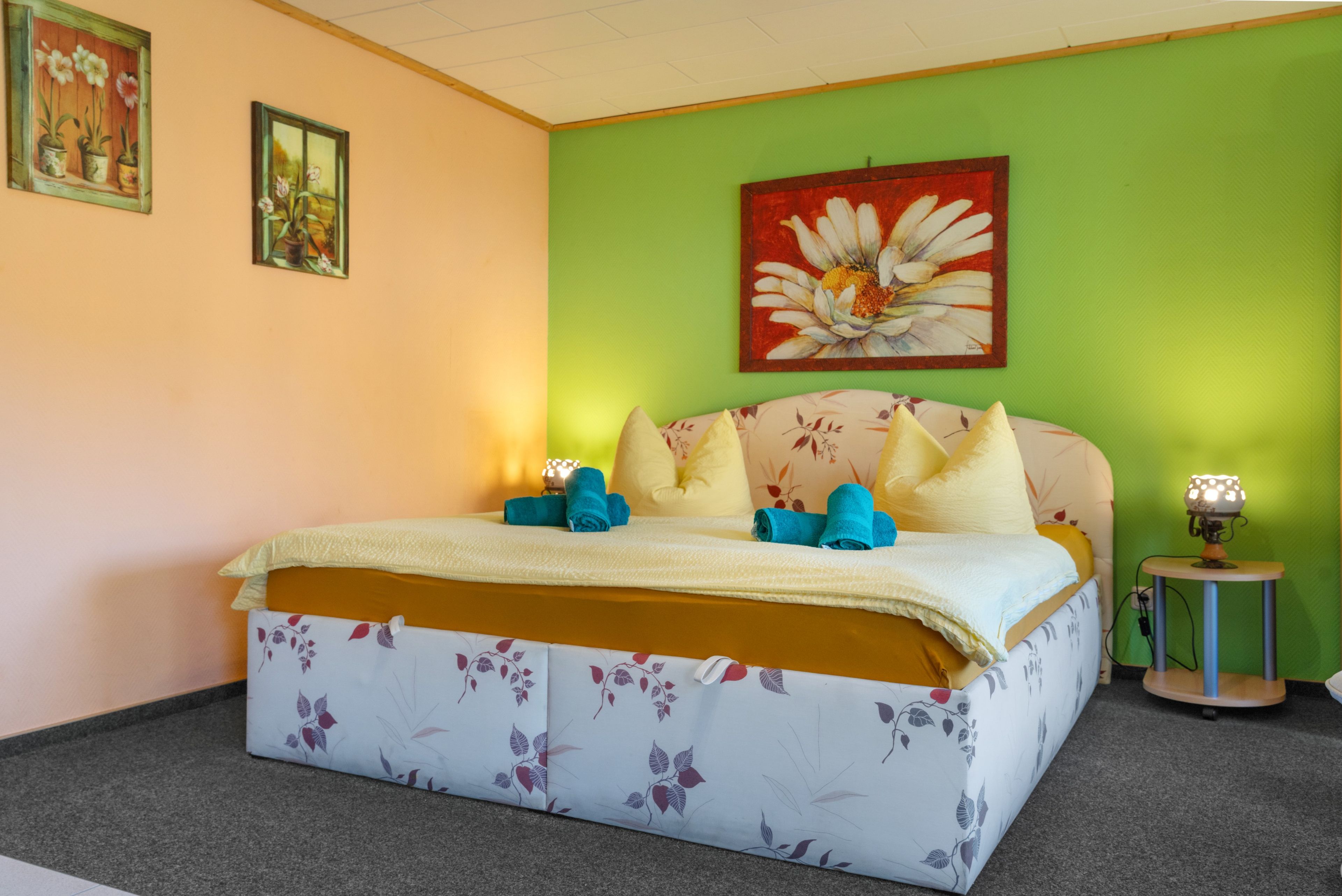 Une chambre à coucher avec une couvre-lit à motifs floraux, un mur vert et un tableau représentant une fleur.
