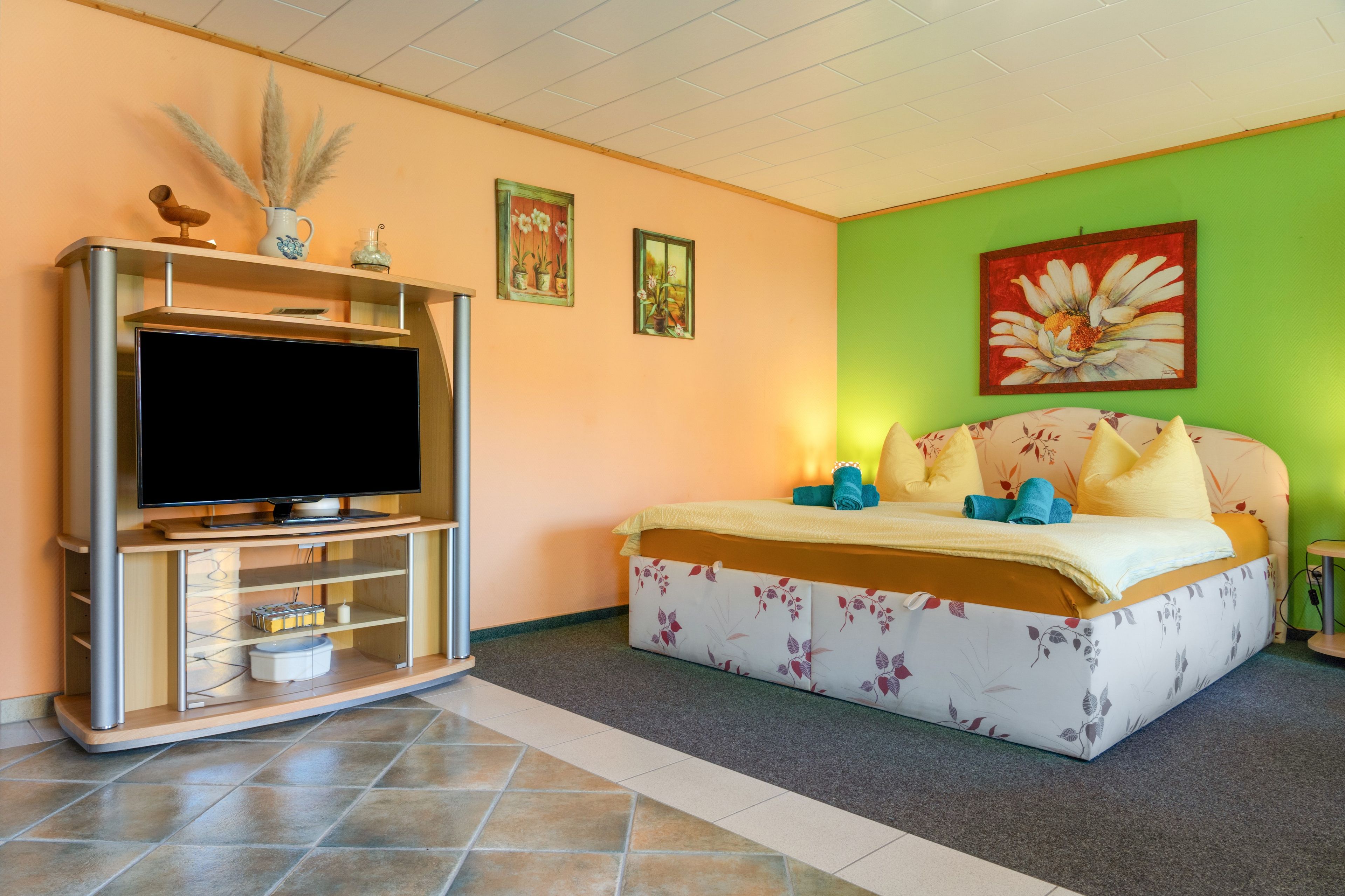 Ein Schlafzimmer mit einem Bett, einem Fernseher und einer Wand mit Kunstwerken.