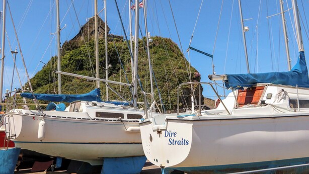 A marina with several sailboats docked, a stone building in the background, and a hill with greenery. - Ocean View (Ilfracombe)