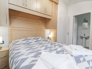 Camera da letto con un letto, una testiera in legno, un comodino, una lampada e un bagno con lavandino e specchio.