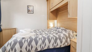 A bedroom with a bed, a nightstand, a wooden wardrobe, and a wall-mounted picture. - Ocean View (Ilfracombe)