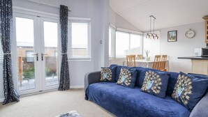 A living room with a blue sofa, patterned curtains, and a dining area with a table and chairs. - Ocean View (Ilfracombe)