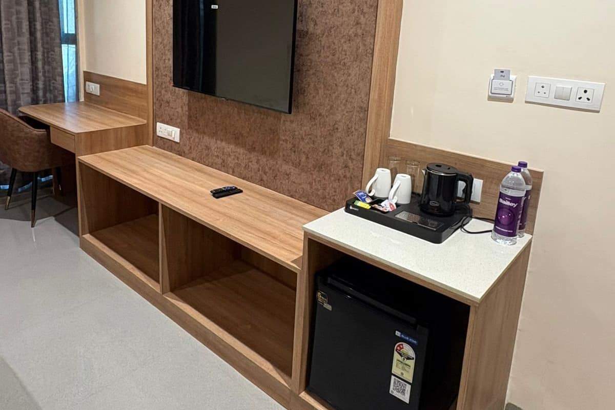 Una camera d'hotel con una scrivania in legno, una TV a schermo piatto montata su una parete strutturata, un piccolo frigorifero e una macchina per il caffè.