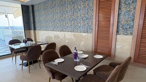 A dining area with a table set for four, surrounded by brown upholstered chairs. - Hotel Maheshwaram Vijay Nagar Indore (Indore)