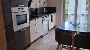 Una cucina moderna con mobili scuri, forno a incasso, macchina per caffè e zona pranzo con tavolo e sedie in vetro.