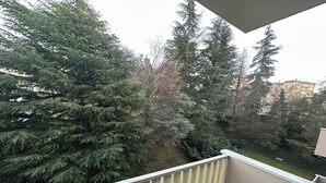 Un balcone con vista su alberi sempreverdi e un edificio in lontananza.