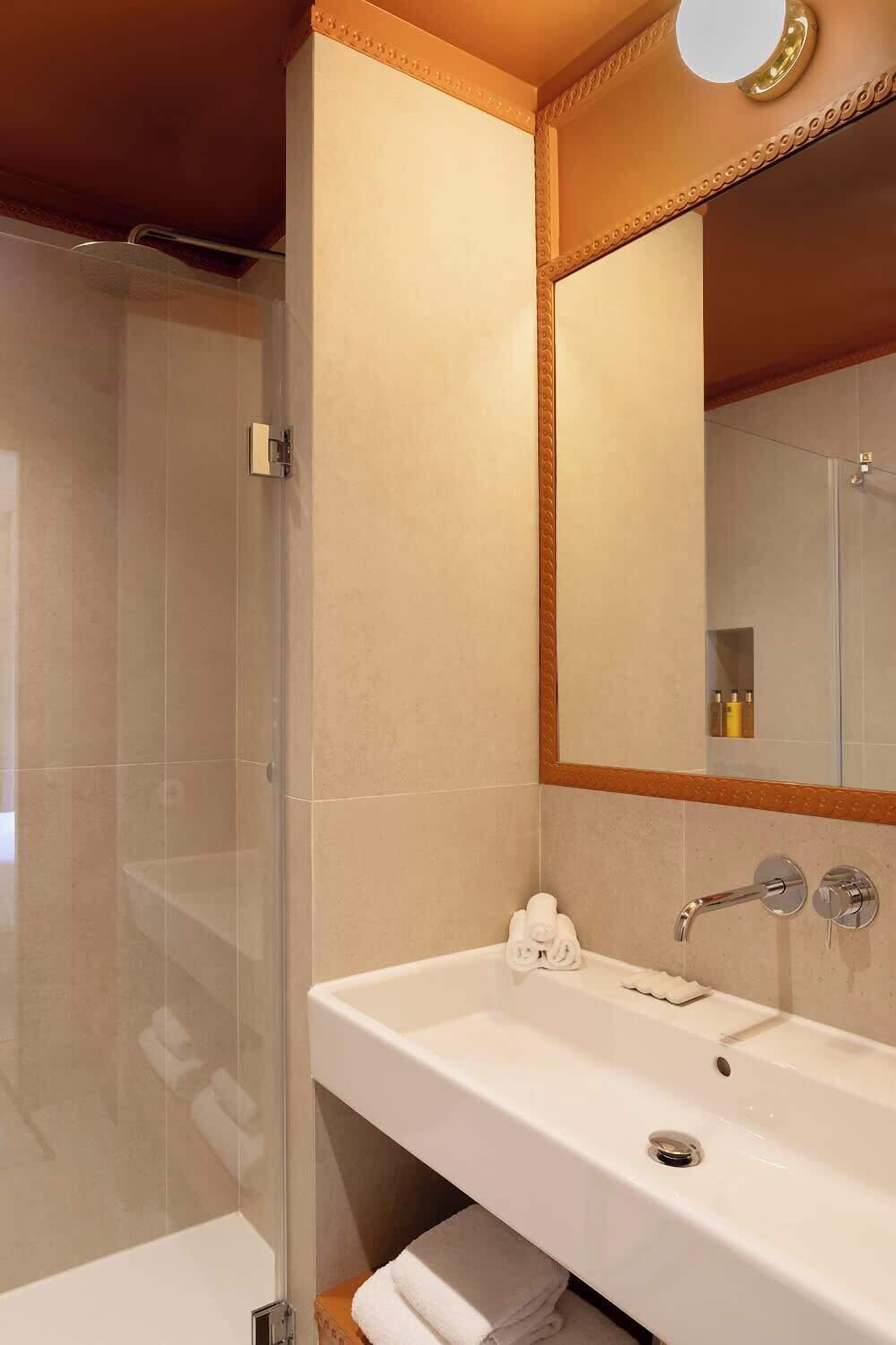 Une salle de bain avec une douche à parois de verre, un lavabo blanc avec un miroir au-dessus et un porte-serviettes en dessous.