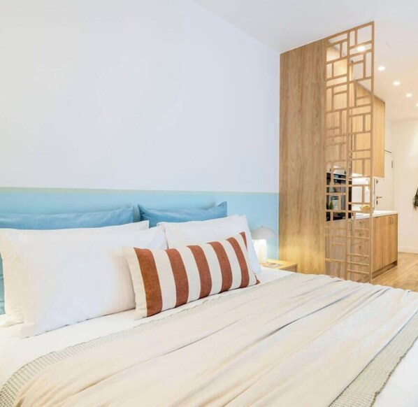 A modern hotel room with a bed, a wooden partition, and a view of the sea. - Stylish Love Nest W/ Balcony in Heart of Koukaki! (Athina)