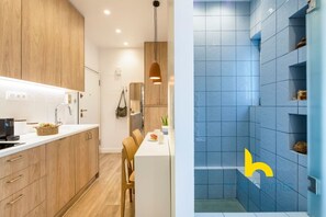 A modern kitchen with wooden cabinets, a white countertop, and a dining area with chairs and a table. - Stylish Love Nest W/ Balcony in Heart of Koukaki! (Athina)