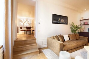 Ein Wohnzimmer mit braunem Sofa, ein Essbereich mit Stühlen und eine Treppe zu einem weiteren Raum.