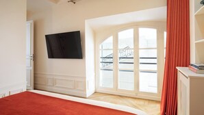 Un dormitori amb un llit gran, un televisor fixat a la paret, una finestra amb vista a una escala i una cortina vermella.