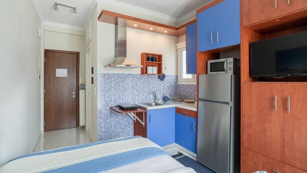 A compact hotel room with a kitchenette, a bed with a blue and white striped bedspread, and a television on a wooden cabinet. - Romantic Island in the Sky, Acropolis & City Views (Athina)