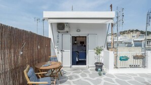 A rooftop terrace with a wooden table and chairs, a potted plant, and a view of the surrounding buildings. - Romantic Island in the Sky, Acropolis & City Views (Athina)