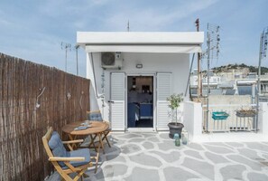 A rooftop terrace with a wooden table and chairs, a potted plant, and a view of the surrounding buildings. - Romantic Island in the Sky, Acropolis & City Views (Athina)