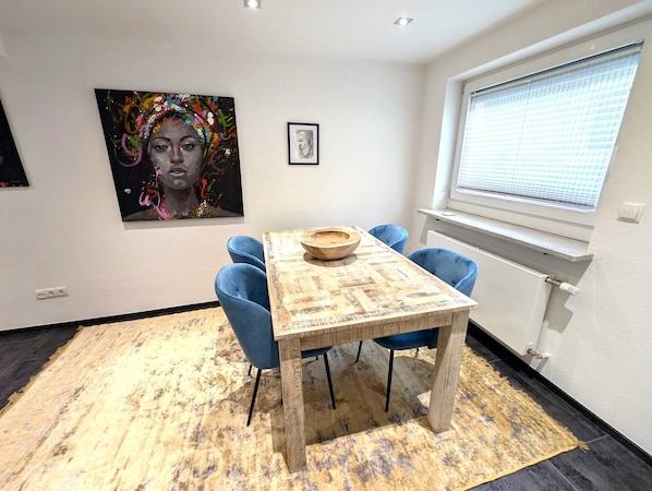 A dining area with a wooden table, blue chairs, and a large abstract painting on the wall.