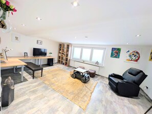 A modern living room with a flat-screen TV, a wooden desk, a black leather sofa, and a small toy car.