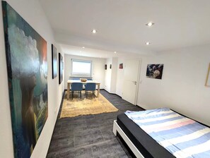 A modern room with a bed, a dining area with chairs, and artwork on the walls.