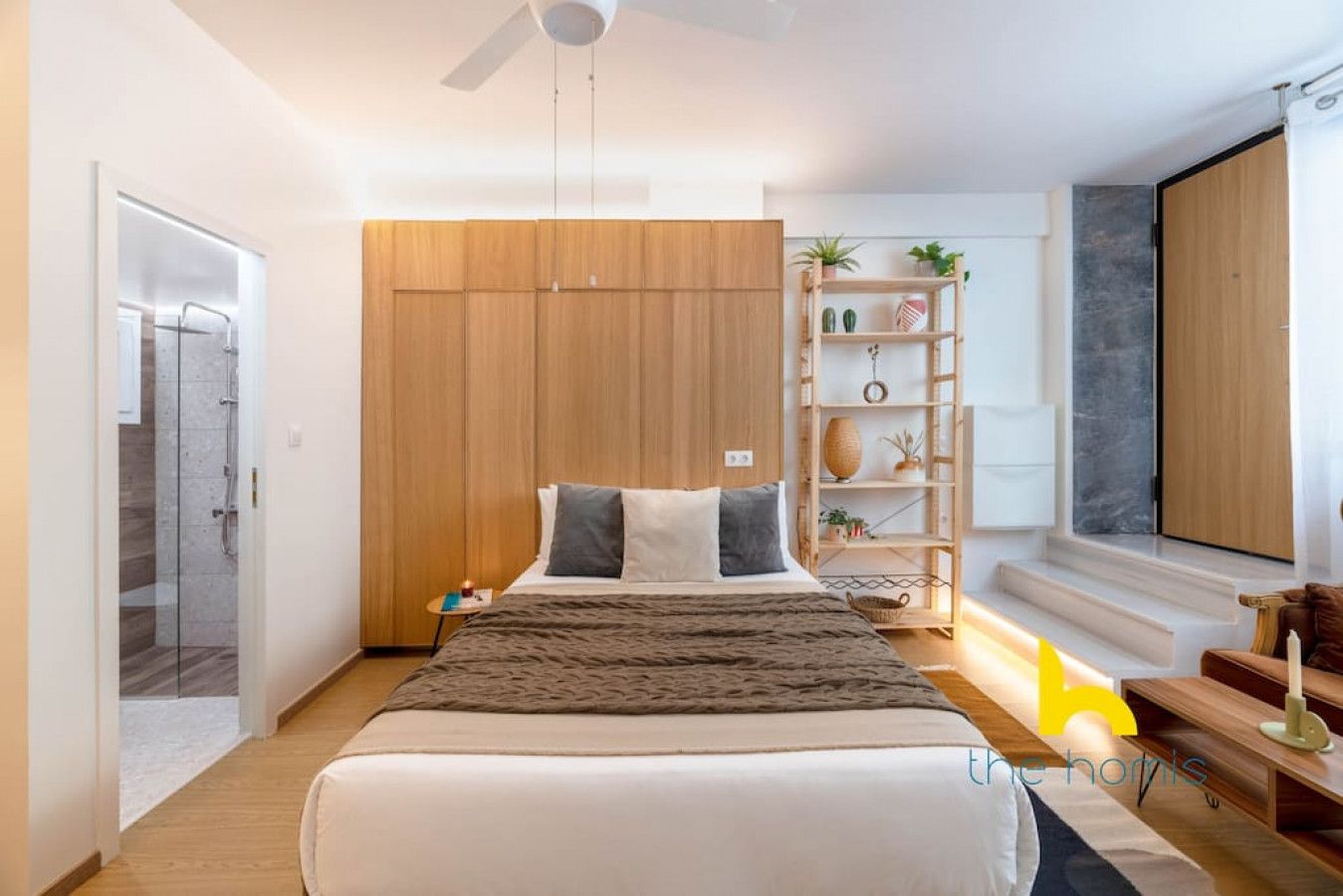 A modern bedroom with a large bed, a wardrobe, a bedside table, a lamp, and a shelf with plants.
