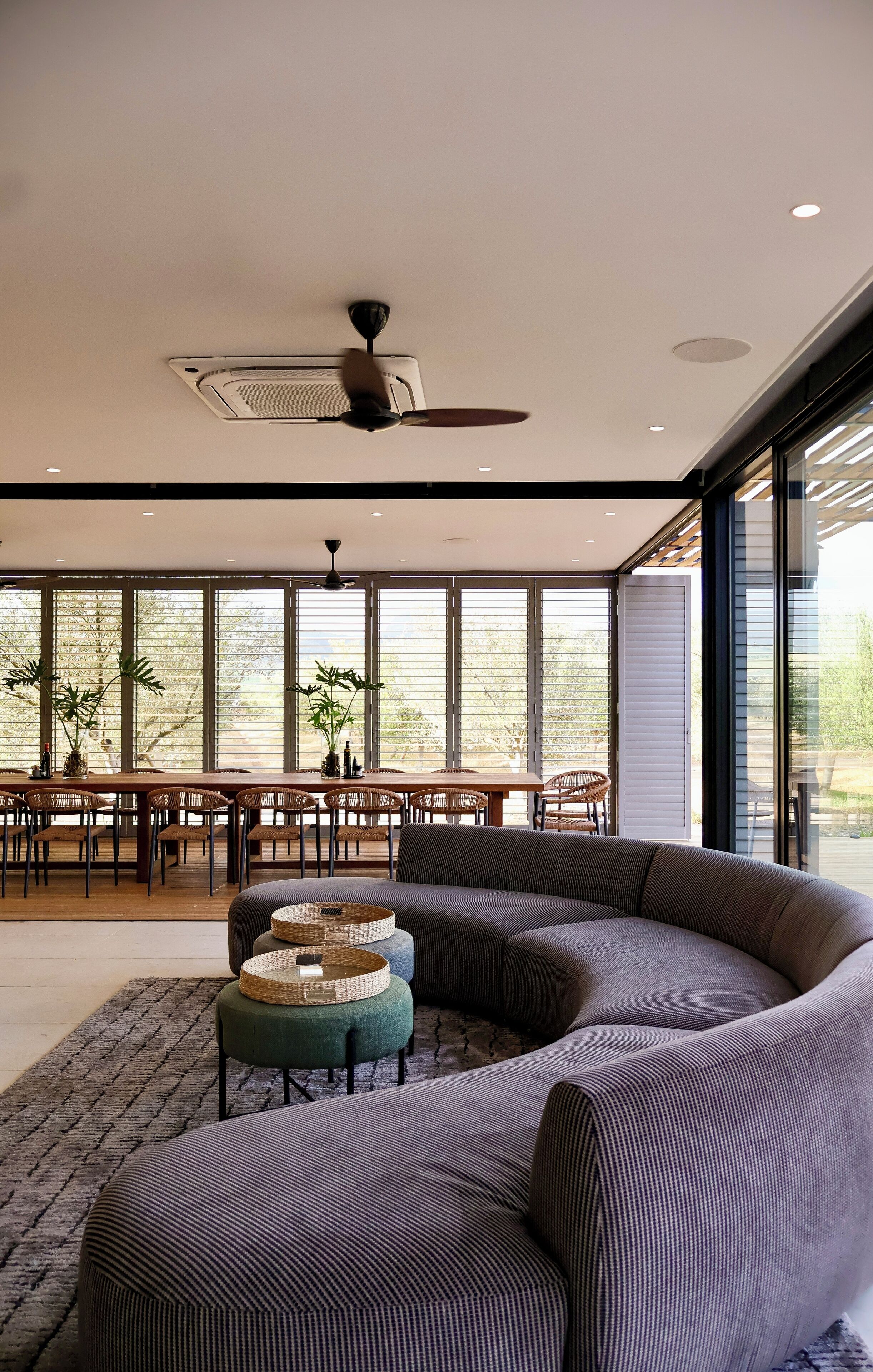 Ein modernes Wohnzimmer mit einer gebogenen Eckcouch, einem Essbereich mit Holztisch und -stühlen sowie großen Fenstern mit Blick ins Freie.