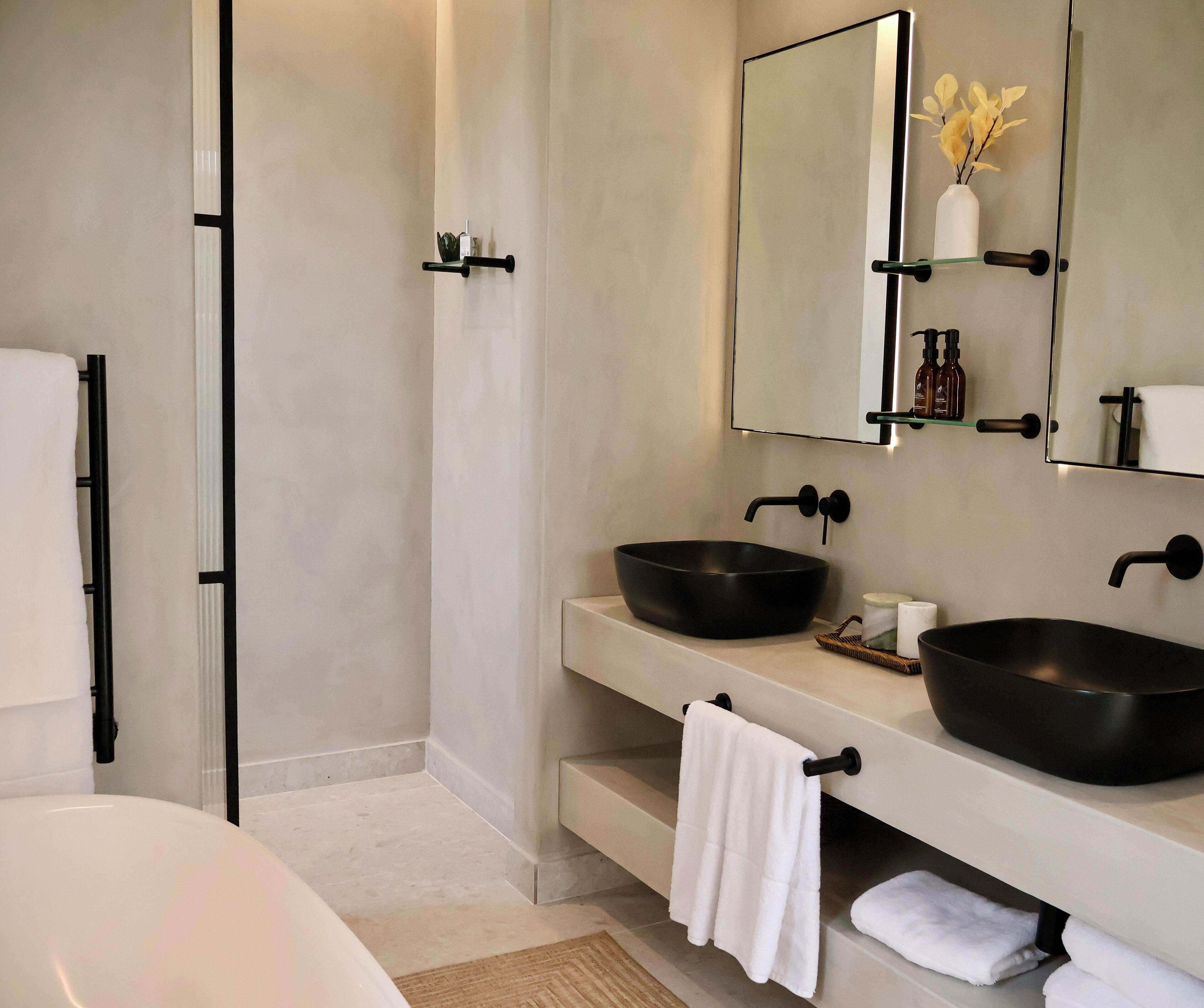 A modern bathroom with a large bathtub, two black vessel sinks, a mirror, and a towel rack.