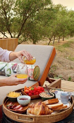 A breakfast tray with croissants, cheese, ham, and fruit on a wicker table outdoors. - Olijvenkraal Winelands Lodge (Paarl)