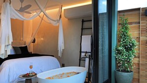A bedroom with a large bed, a bathtub filled with flowers, and a potted plant. - Olijvenkraal Winelands Lodge (Paarl)